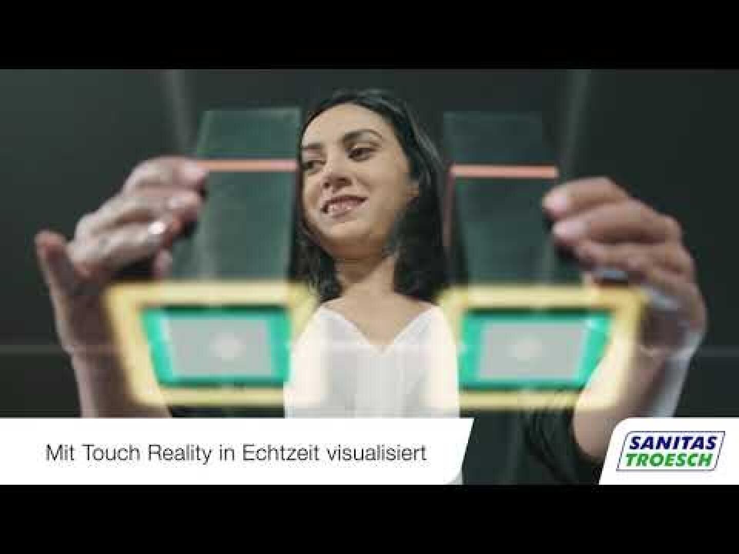 Eine Frau interagiert mit einer virtuellen Touchscreen-Oberfläche und scheint digitale Bedienelemente zu betätigen. Der deutsche Text am unteren Rand lautet: "Mit Touch Reality in Echtzeit visualisiert". Das SANITAS TROESCH-Logo ist in der unteren rechten Ecke zu sehen.