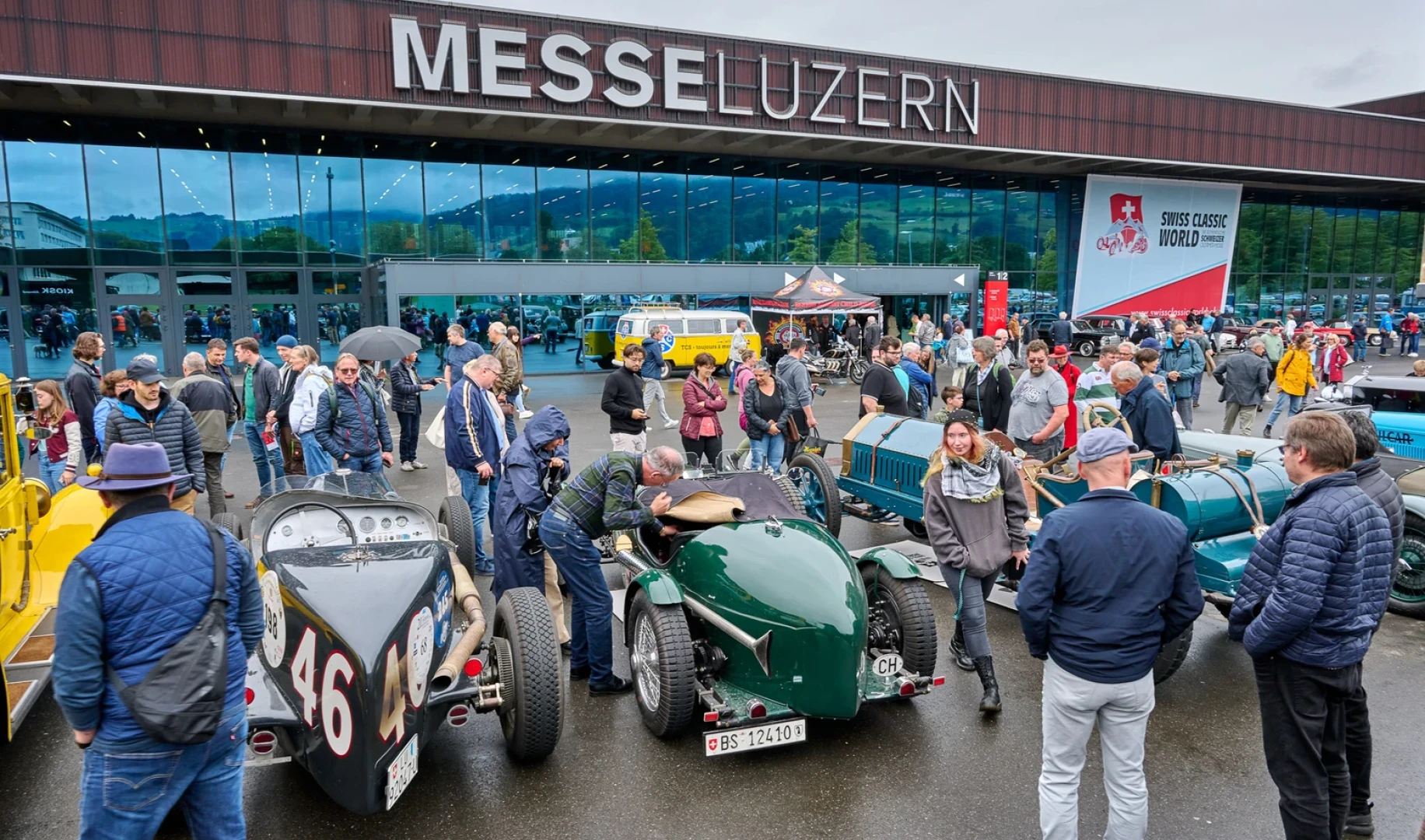 Vor der Messe Luzern versammelt sich eine Menschenmenge, um sich die ausgestellten Oldtimer bei einer Oldtimer-Veranstaltung anzusehen. Unter bewölktem Himmel werden die Fahrzeuge begutachtet und Fotos gemacht.