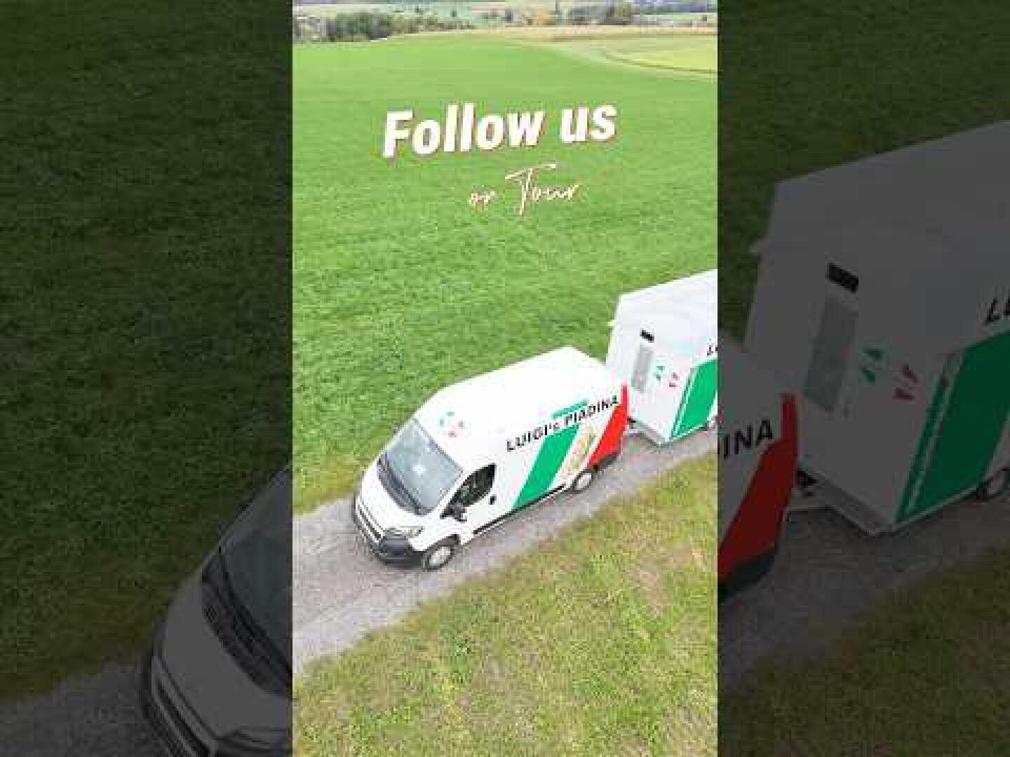 Ein weißer Lieferwagen mit grünen und roten Streifen fährt auf einer Straße durch grasbewachsene Felder. Der Text über dem Van lautet "Follow us on Tour". Andere Fahrzeuge sind teilweise in der Nähe zu sehen.