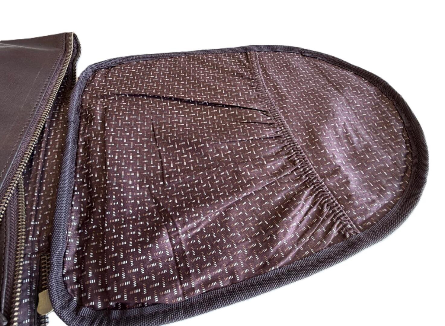 Nahaufnahme einer offenen braunen Reißverschlusstasche mit einem gemusterten Stofffutter und elastischen Innentaschen auf weißem Hintergrund.