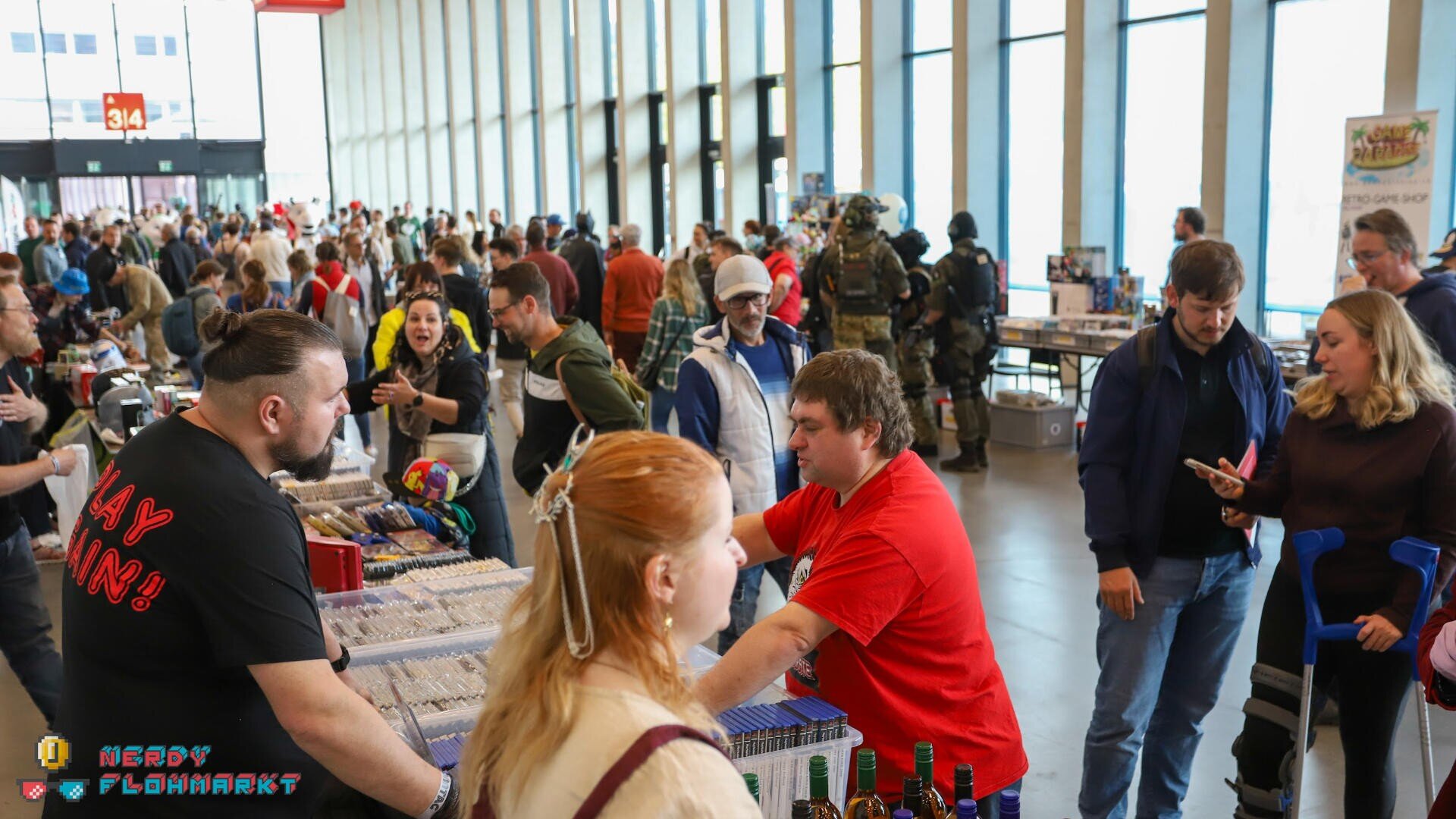 Menschenmassen stöbern an den Tischen der Anbieter von Comics und Sammlerstücken auf einer Messe. In einer großen, hell erleuchteten Halle mit hohen Fenstern wird geplaudert und eingekauft, manche in Verkleidung.