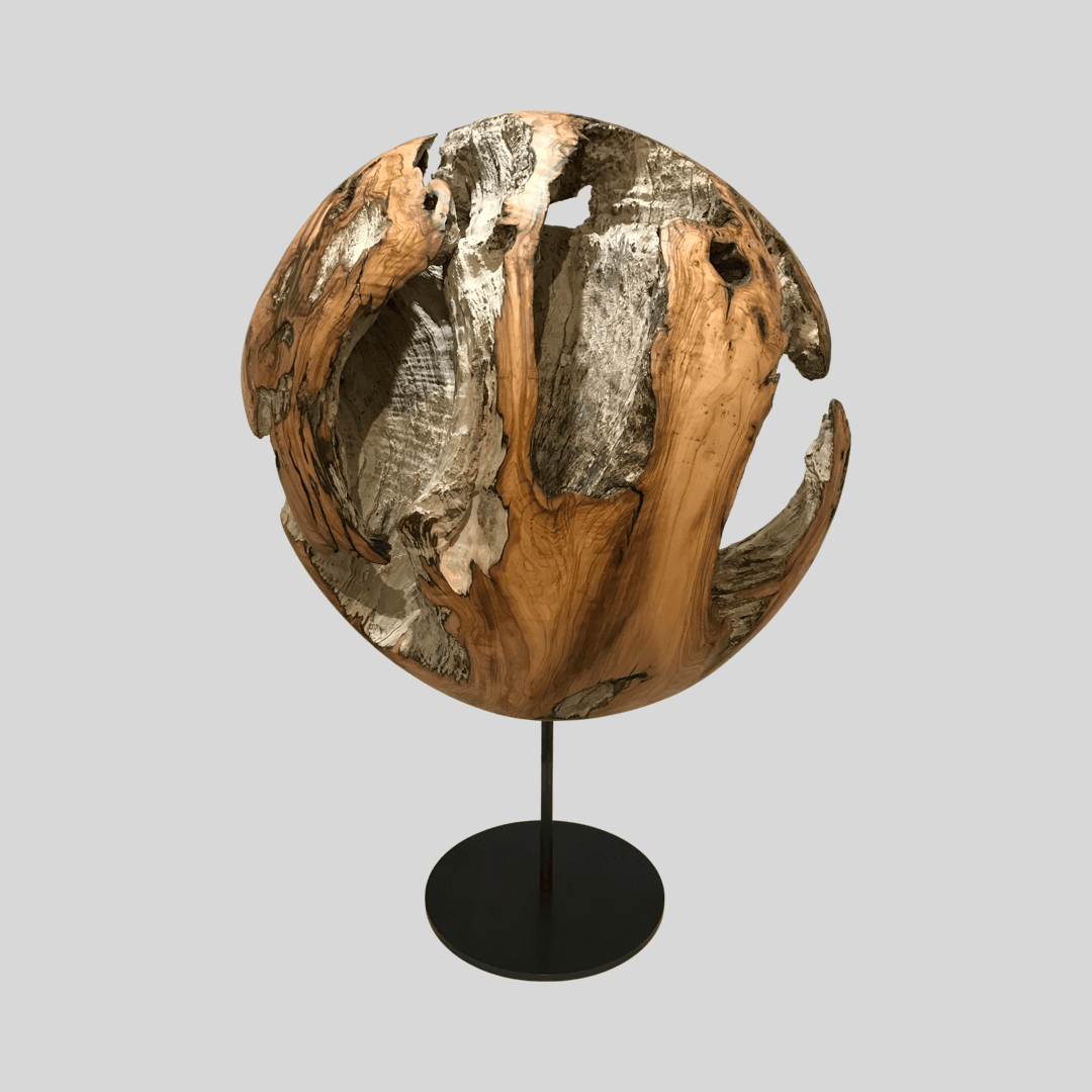 Ein skulpturaler Holzglobus mit großen, unregelmäßigen Ausschnitten und strukturierten Oberflächen, montiert auf einem einfachen schwarzen Metallständer vor einem schlichten hellgrauen Hintergrund.