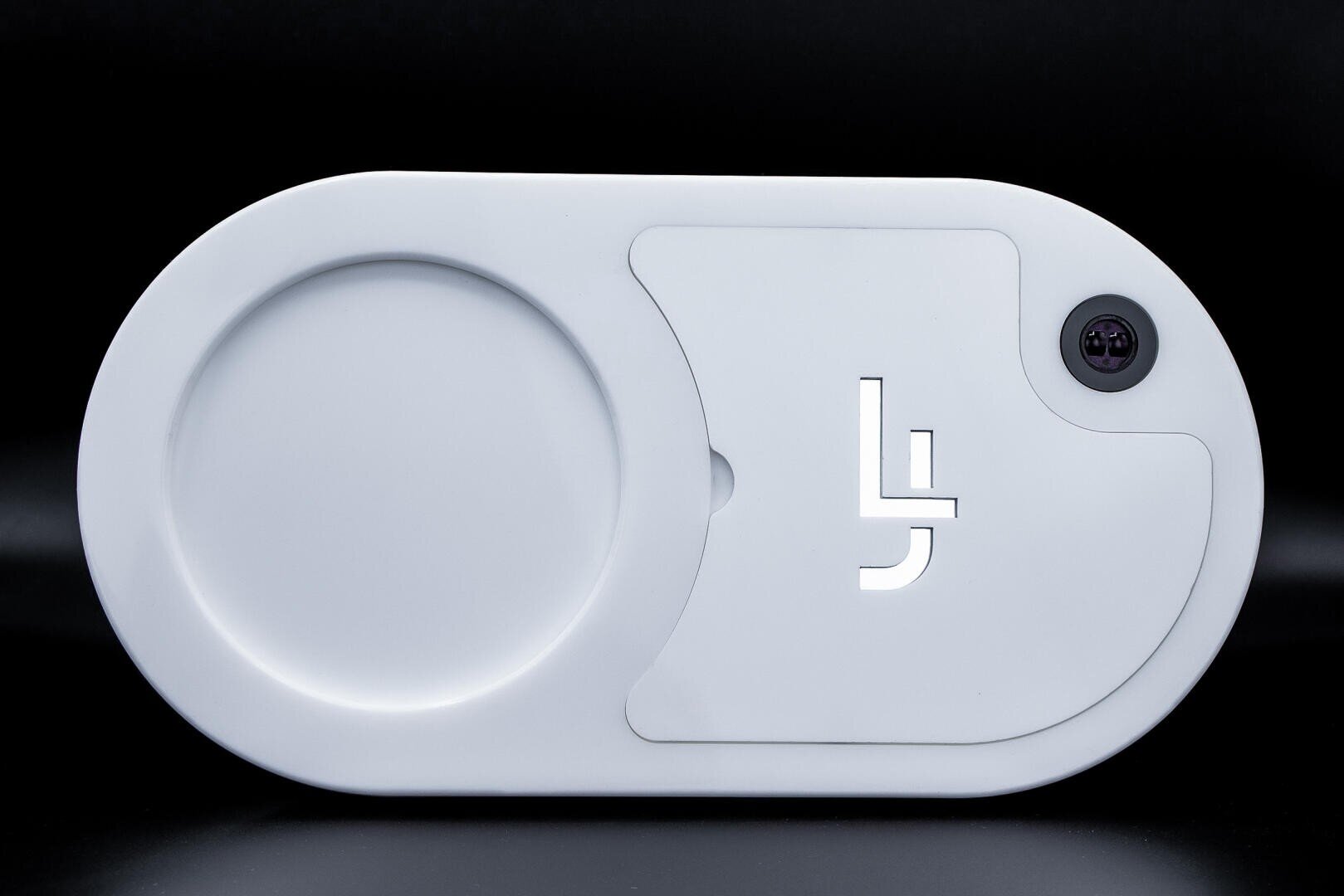 Ein schlankes, ovales, weißes Gerät mit einer kreisförmigen Vertiefung auf der linken Seite und einer kleinen Kameralinse auf der oberen rechten Seite. Ein stilisiertes LJ-Logo ist in der Nähe der Mitte ausgeschnitten. Der Hintergrund ist einfarbig schwarz.