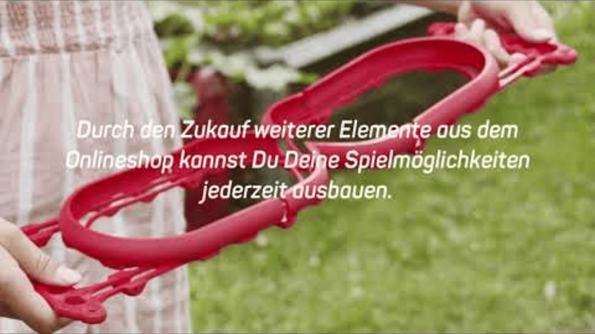 Eine Person in einem hellen Kleid hält im Freien ein rotes Plastikspielzeug. Der deutsche Text über dem Bild erwähnt die Erweiterung der Spielmöglichkeiten durch den Kauf zusätzlicher Elemente in einem Online-Shop.