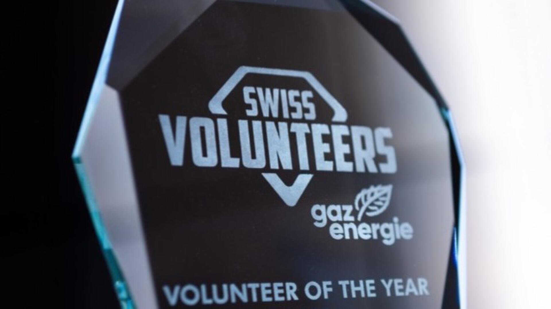 Ein Glaspreis mit der Gravur Swiss Volunteers gaz energie und Volunteer of the Year auf dunklem Hintergrund.