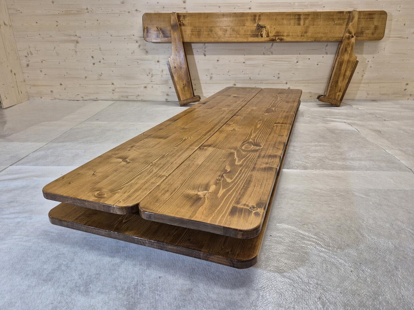 In einem Raum mit hellen, holzgetäfelten Wänden stehen ein Holztisch und eine Bank mit polierter Oberfläche auf einem hellen, kunststoffbeschichteten Boden.