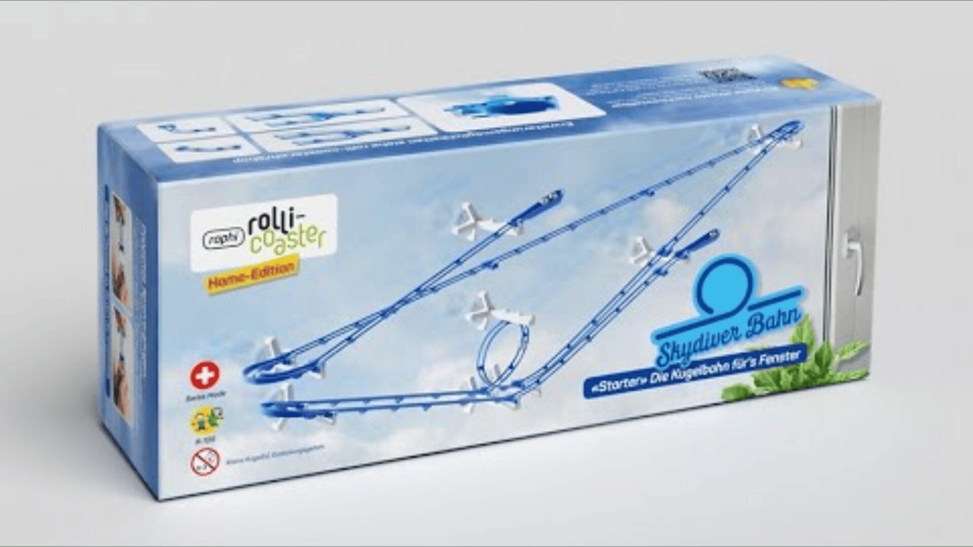 Eine rechteckige Schachtel mit blauer und weißer Grafik, die ein Murmel-Achterbahn-Spielzeugset mit der Bezeichnung rolli-coaster Home-Edition Skydiver Bahn zeigt, mit einer gewundenen Kunststoffbahn und Murmeln auf der Vorderseite der Verpackung.
