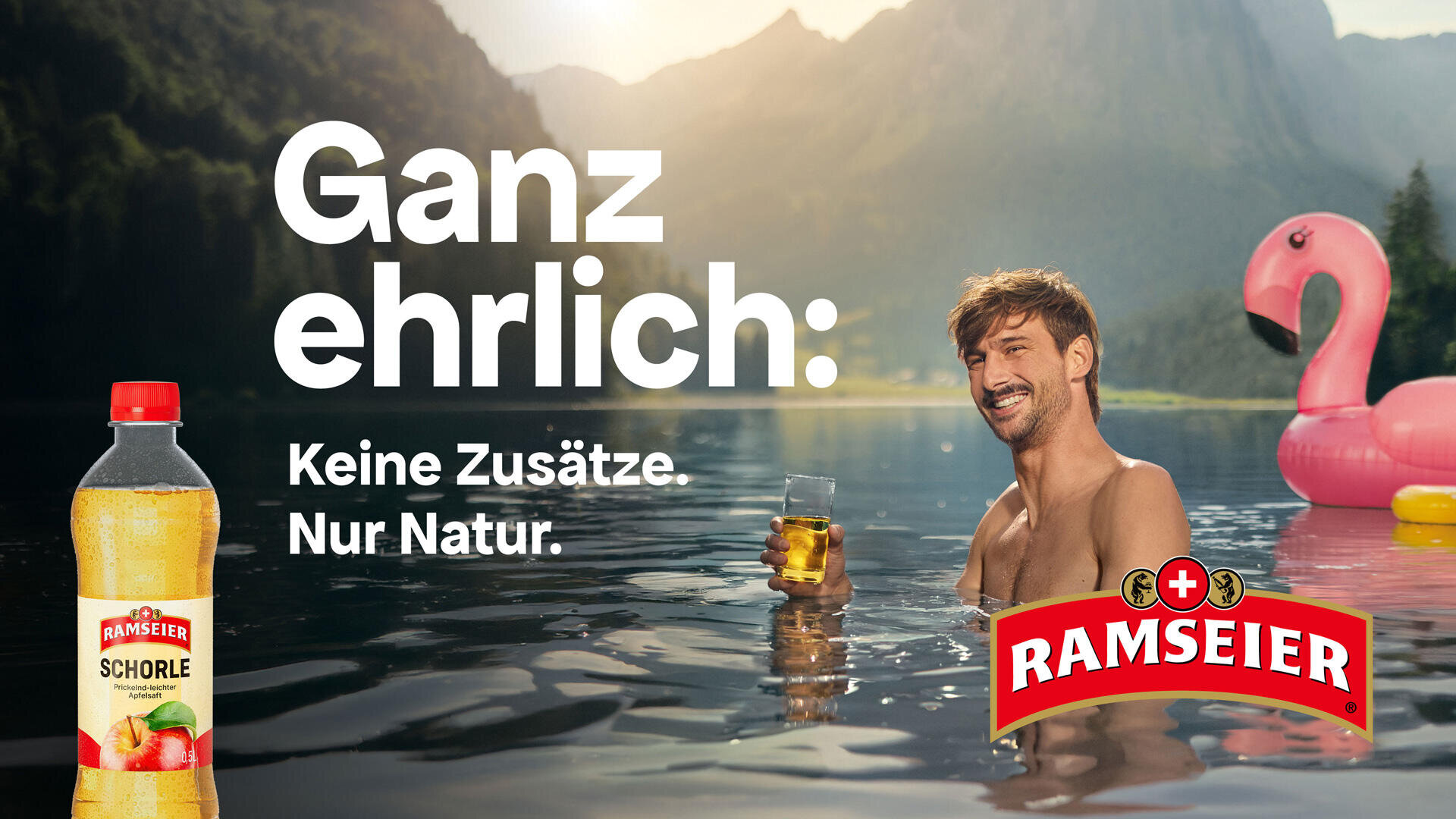 Ein lächelnder Mann entspannt sich mit einem Getränk in der Hand in einem See, in dessen Nähe ein rosa Flamingo schwimmt. In der Nähe schwimmt ein rosa Flamingo. Die Flasche und das Logo von Ramseier Schorle sowie der deutsche Text werben für natürliche Inhaltsstoffe und ohne Zusatzstoffe. Bewaldete Hügel und Sonnenlicht im Hintergrund.