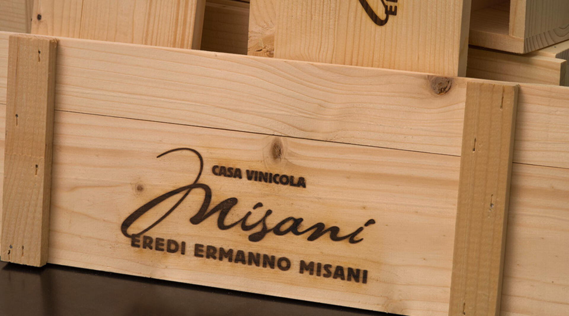 Weinkiste aus Holz mit dem Logo Casa Vinicola Misani Eredi Ermanno Misani, das in fetter Schrift auf die Seite geätzt ist. Die Kiste hat vertikale Holzlatten an den Ecken für die Unterstützung.