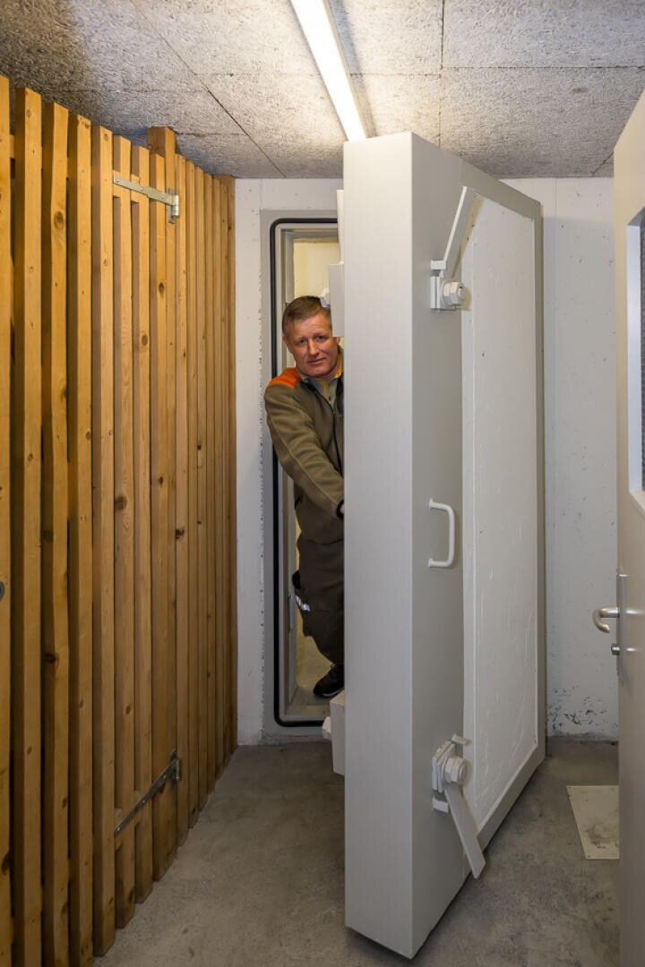 Ein Mann in Uniform steht in einer dicken, schweren Tür, möglicherweise einer Sprengtür, in einem Betonraum mit Holzverkleidung auf einer Seite und Leuchtstoffröhren über dem Kopf.