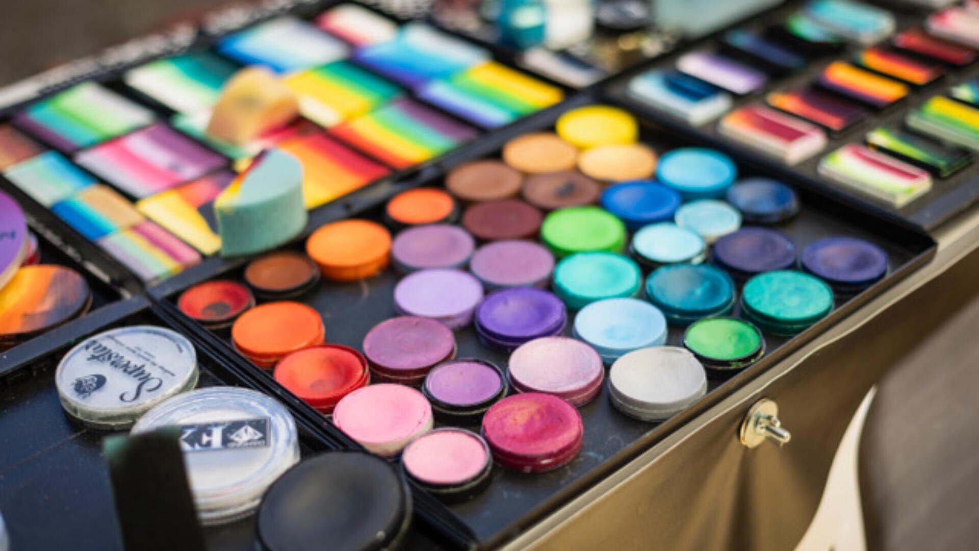 Nahaufnahme eines Schminkkastens mit einer Vielzahl von bunten Lidschatten, Gesichtsfarben und Make-up-Schwämmen, die ordentlich in runden und rechteckigen Pfännchen angeordnet sind.