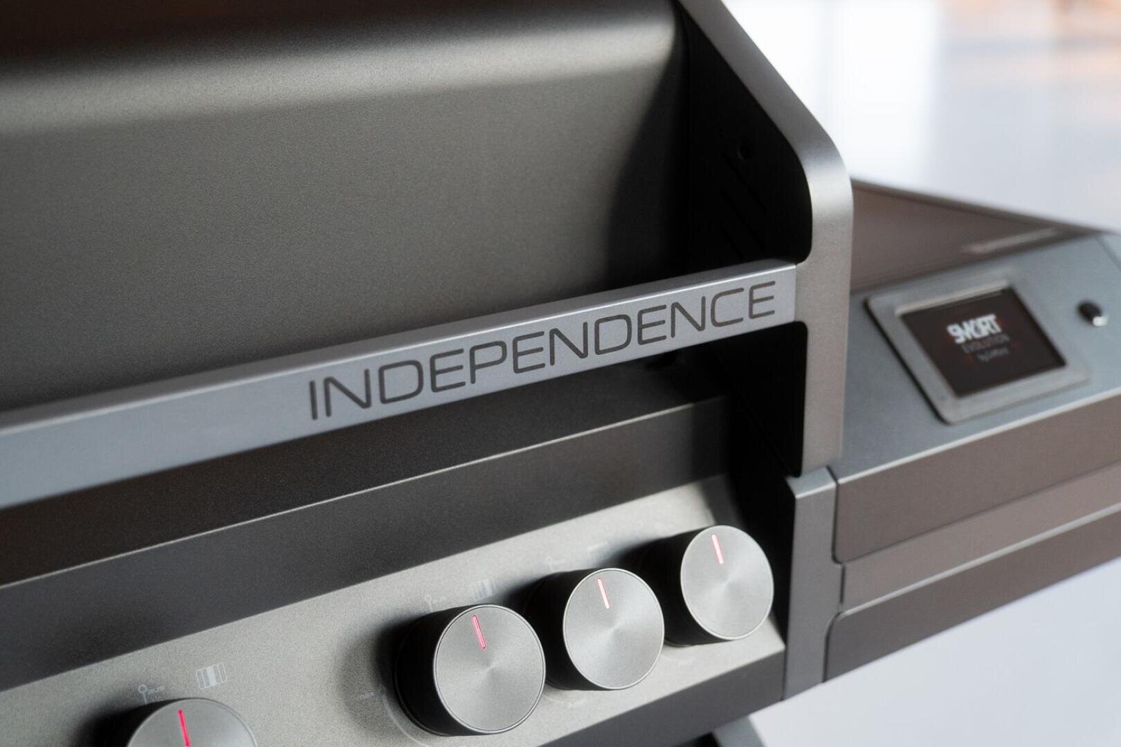 Nahaufnahme eines modernen Grills mit der Aufschrift „INDEPENDENCE“ auf dem vorderen Griff, vier Bedienknöpfen darunter und einem digitalen Display auf der rechten Seite.