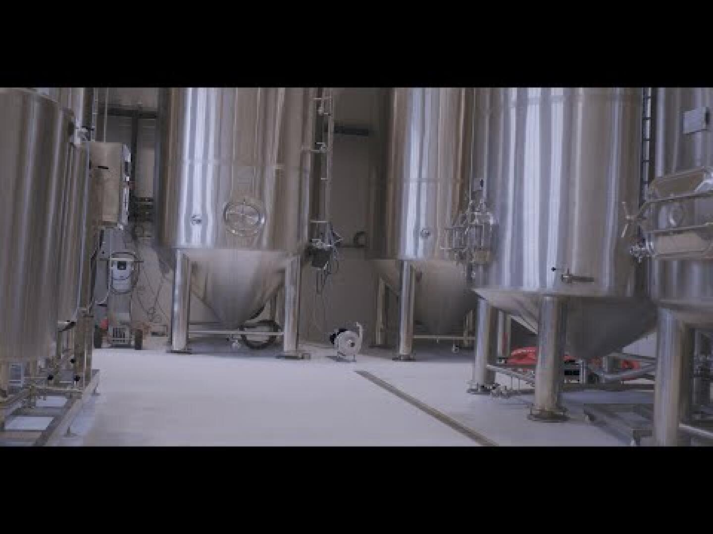 Große Edelstahltanks und -ausrüstungen in einer modernen Industrieanlage, wahrscheinlich einer Brauerei oder einem lebensmittelverarbeitenden Betrieb, mit einem sauberen, hellen Boden und metallischen Oberflächen.