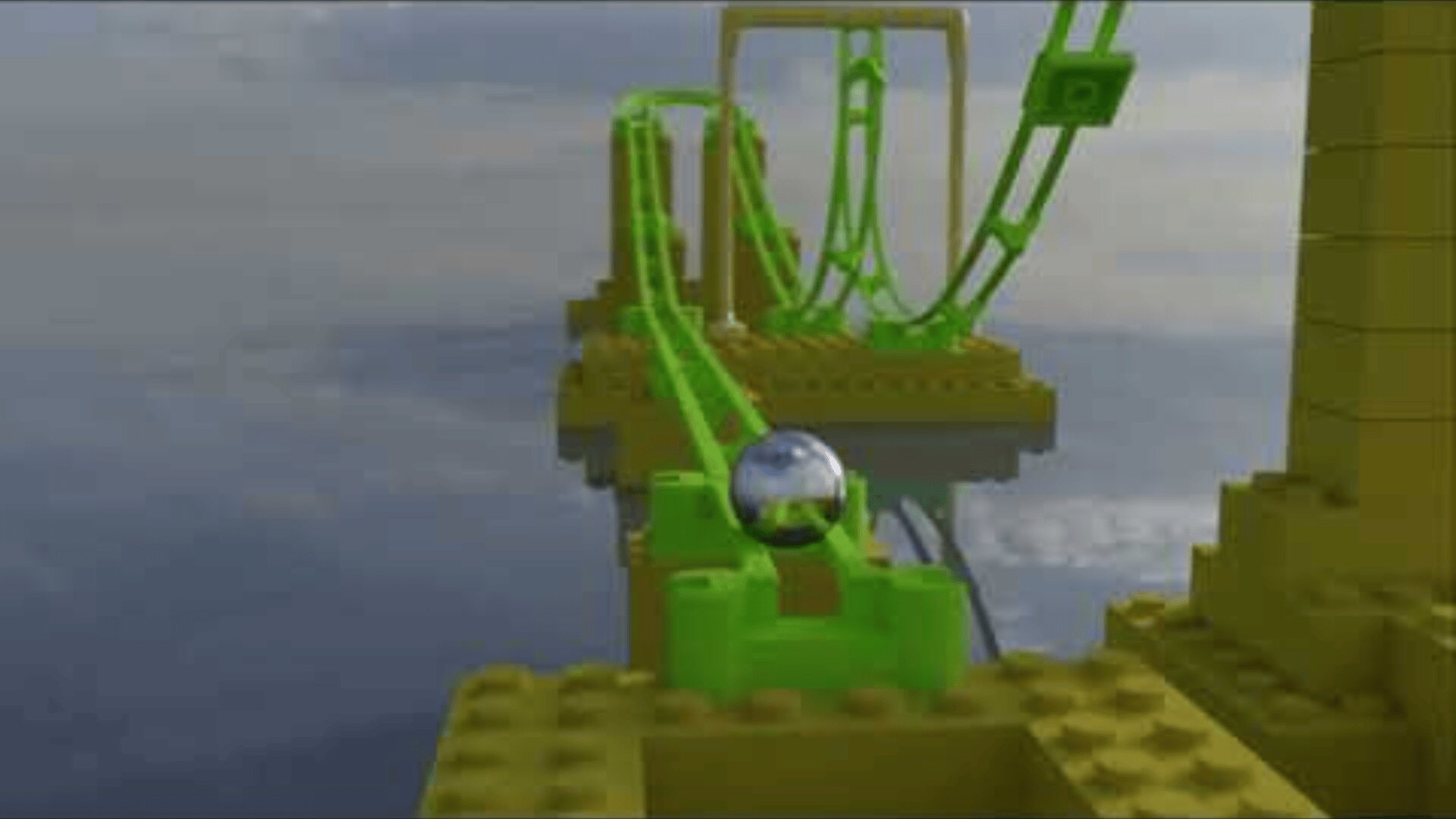 Eine metallisch glänzende Kugel rollt eine leuchtend grüne LEGO Achterbahnstrecke hinunter, umgeben von gelben LEGO Strukturen vor einem wolkenverhangenen Himmel.