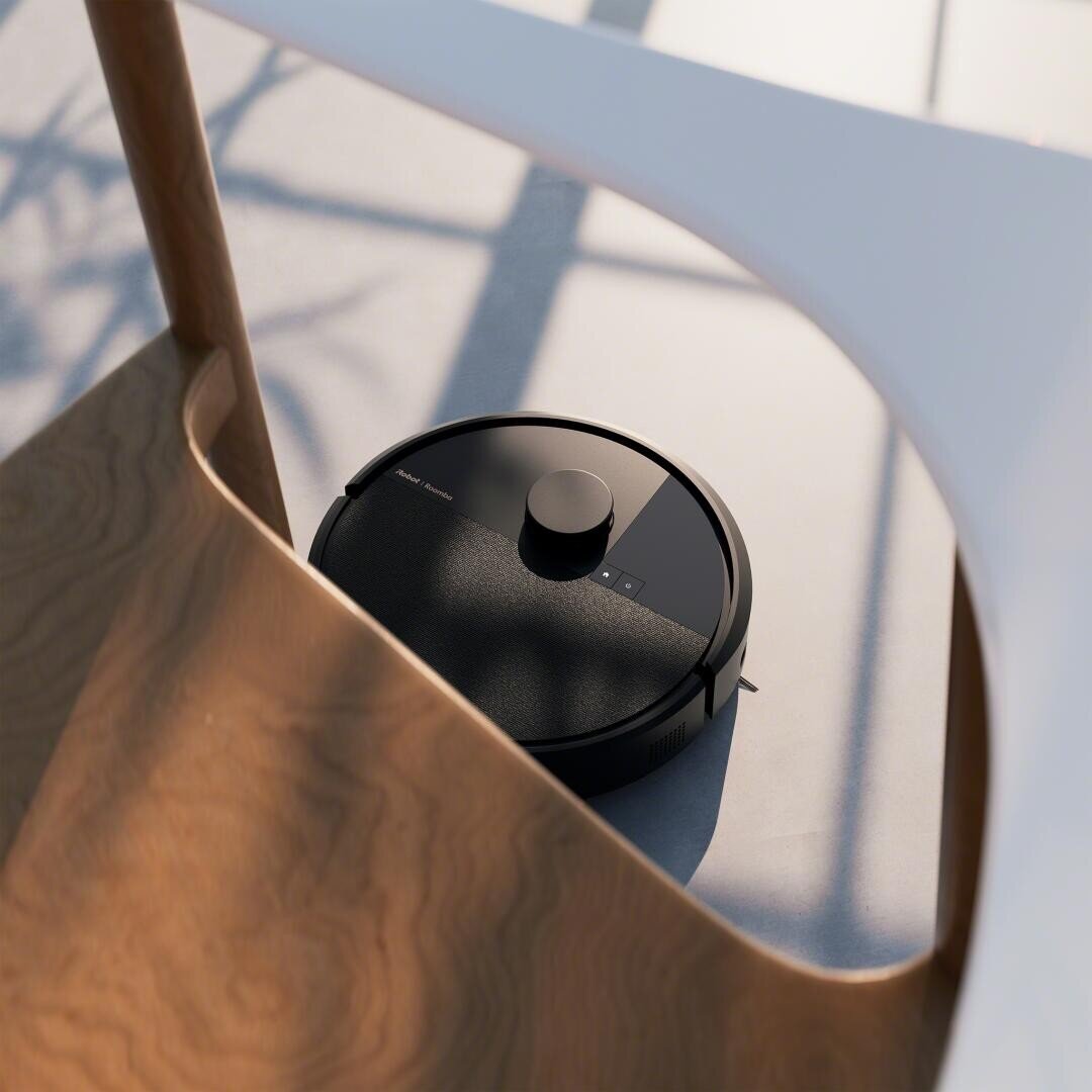 Ein schwarzer Staubsaugerroboter fährt in einem sonnenbeschienenen Raum über einen hellen Boden, teilweise unter einem Holzstuhl mit weißen Beinen.