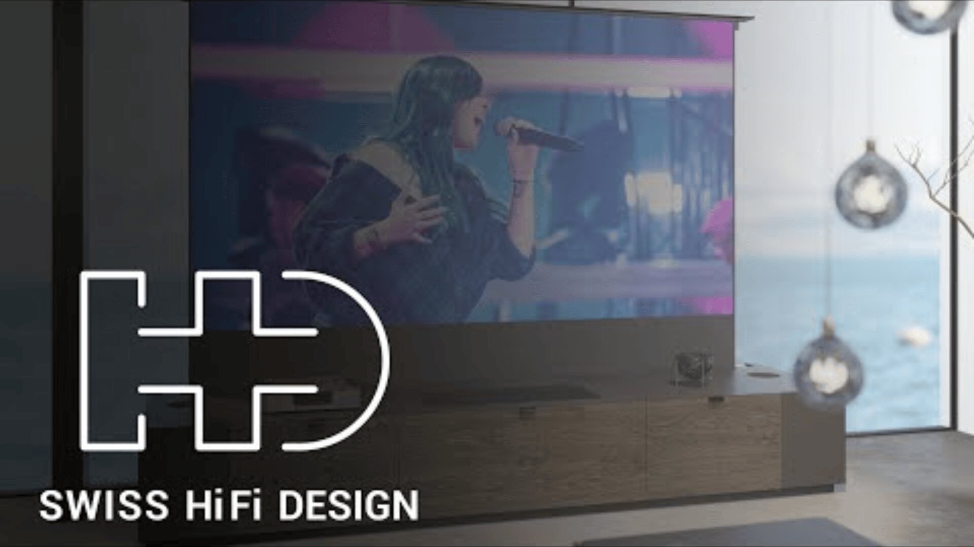 Ein großer Fernsehbildschirm zeigt eine singende Frau auf der Bühne. Der Raum ist modern eingerichtet und bietet einen Blick aufs Meer. Der Schriftzug SWISS HiFi DESIGN und ein Logo sind in der unteren linken Ecke zu sehen.
