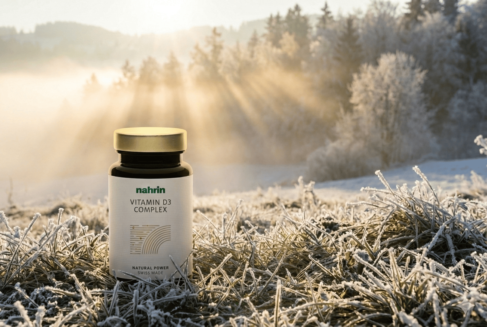 Eine Flasche Nahrin Vitamin D3 Complex steht bei Sonnenaufgang auf dem frostigen Gras, während das Sonnenlicht durch die Bäume im Hintergrund die neblige Landschaft erhellt.