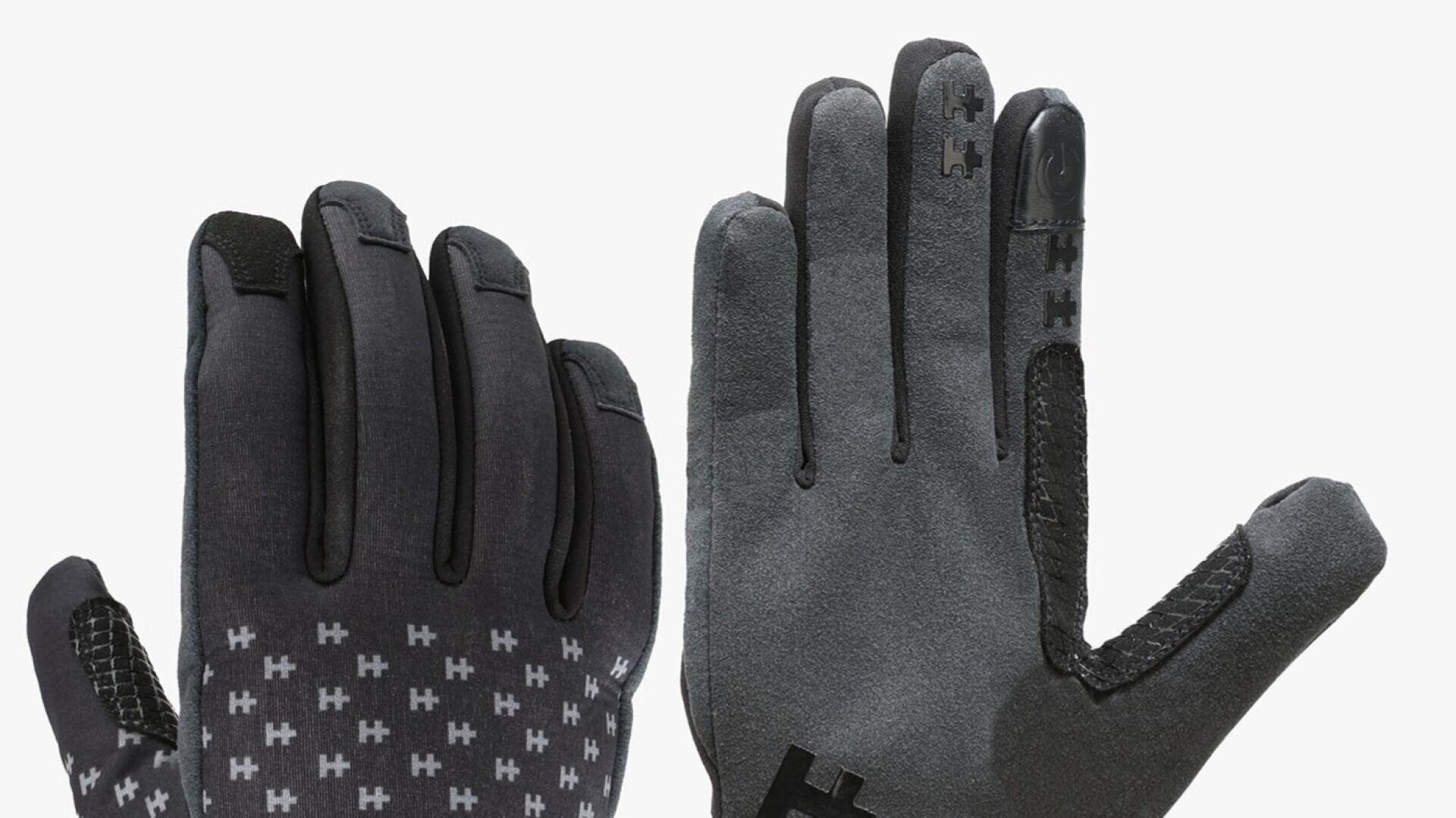 Ein Paar graue Handschuhe mit schwarzen Akzenten, mit griffigen Mustern aus kleinen H-Formen auf der Handfläche und den Fingern sowie Touchscreen-kompatiblen Spitzen an Zeigefinger und Daumen.
