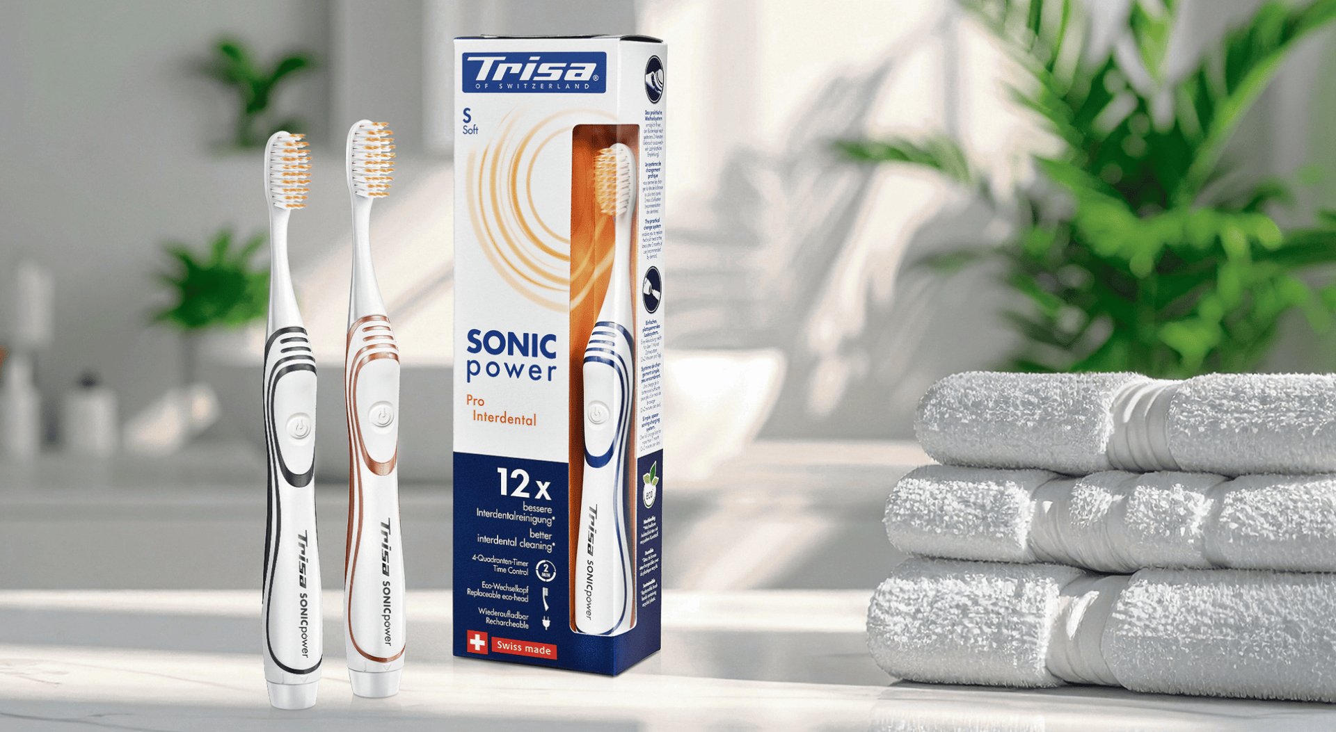 Zwei Trisa Sonic Power elektrische Zahnbürsten, eine mit blauen und eine mit roten Akzenten, stehen neben ihrer Verpackung auf einem Badezimmertisch mit gestapelten weißen Handtüchern im Hintergrund.