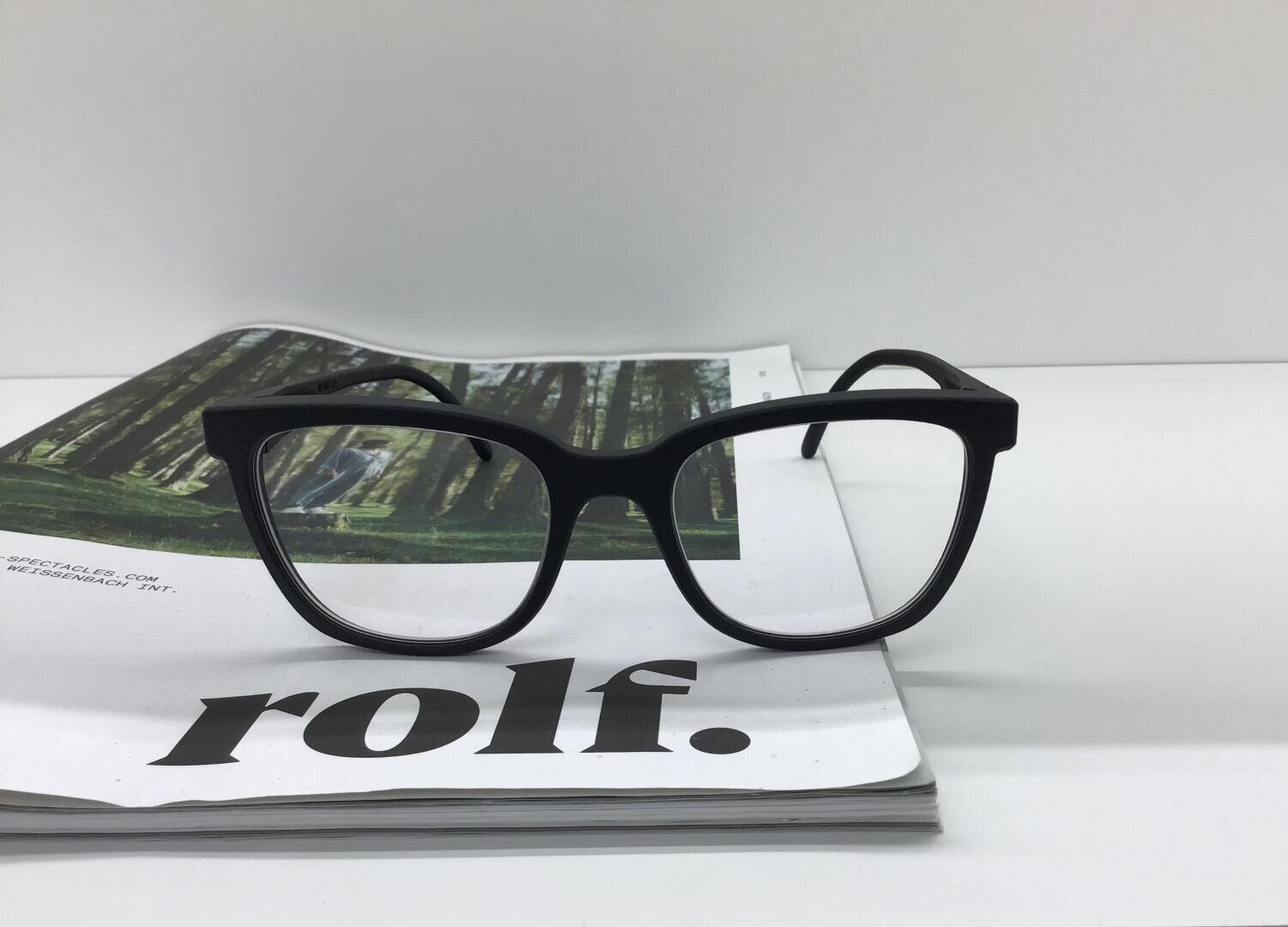 Eine schwarze Brille liegt auf einem aufgeschlagenen Magazin. Auf der Seite steht unten in fetten Buchstaben das Wort rolf. und oben ein Foto eines Waldes. Der Hintergrund ist weiß.