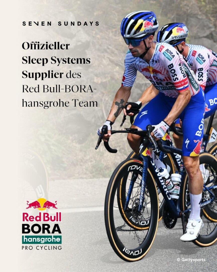 Zwei Radprofis des Teams Red Bull-BORA-hansgrohe fahren auf Rennrädern in einem Wettkampf. Neben ihnen kündigt ein Text Seven Sundays als offiziellen Schlafsystem-Lieferanten für das Team an.