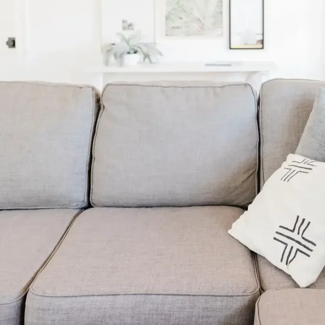Eine Nahaufnahme eines hellgrauen Sofas mit einem weißen Zierkissen mit schwarzen geometrischen Mustern in einem hellen, minimalistischen Wohnzimmer mit einer weißen Wand und gerahmter Kunst im Hintergrund.