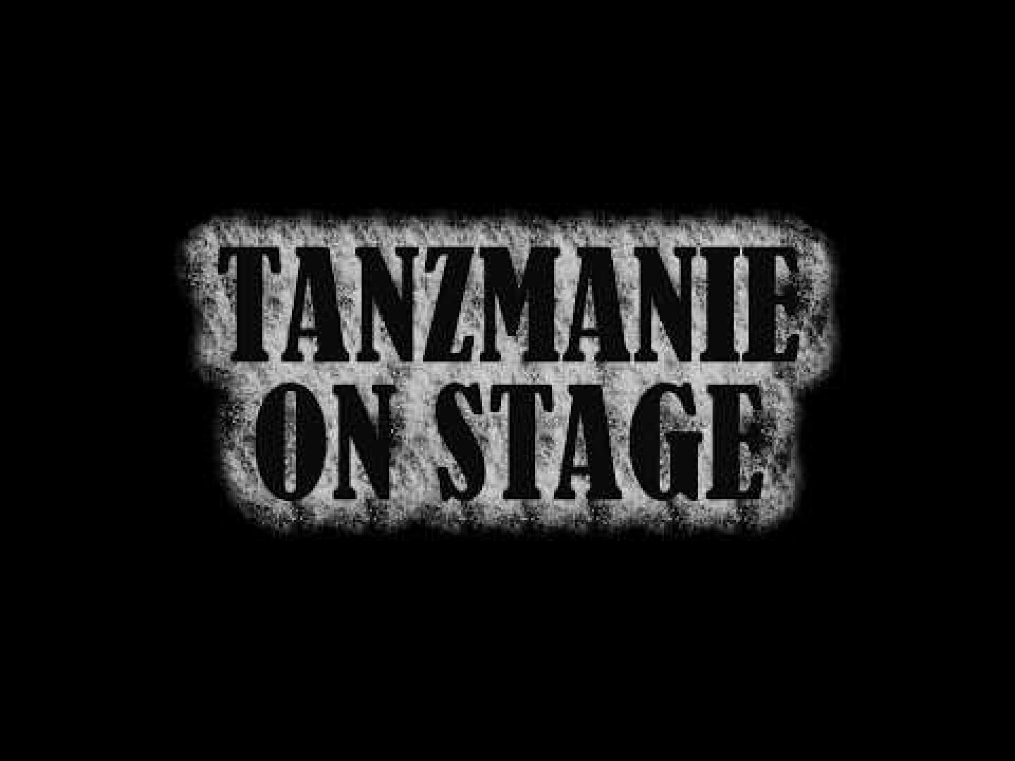 Der Text lautet TANZMANIE ON STAGE in fetten, schwarzen Schablonenbuchstaben mit Grunge-Effekt auf einem gesprenkelten grauen Hintergrund, zentriert auf einem soliden schwarzen Hintergrund.