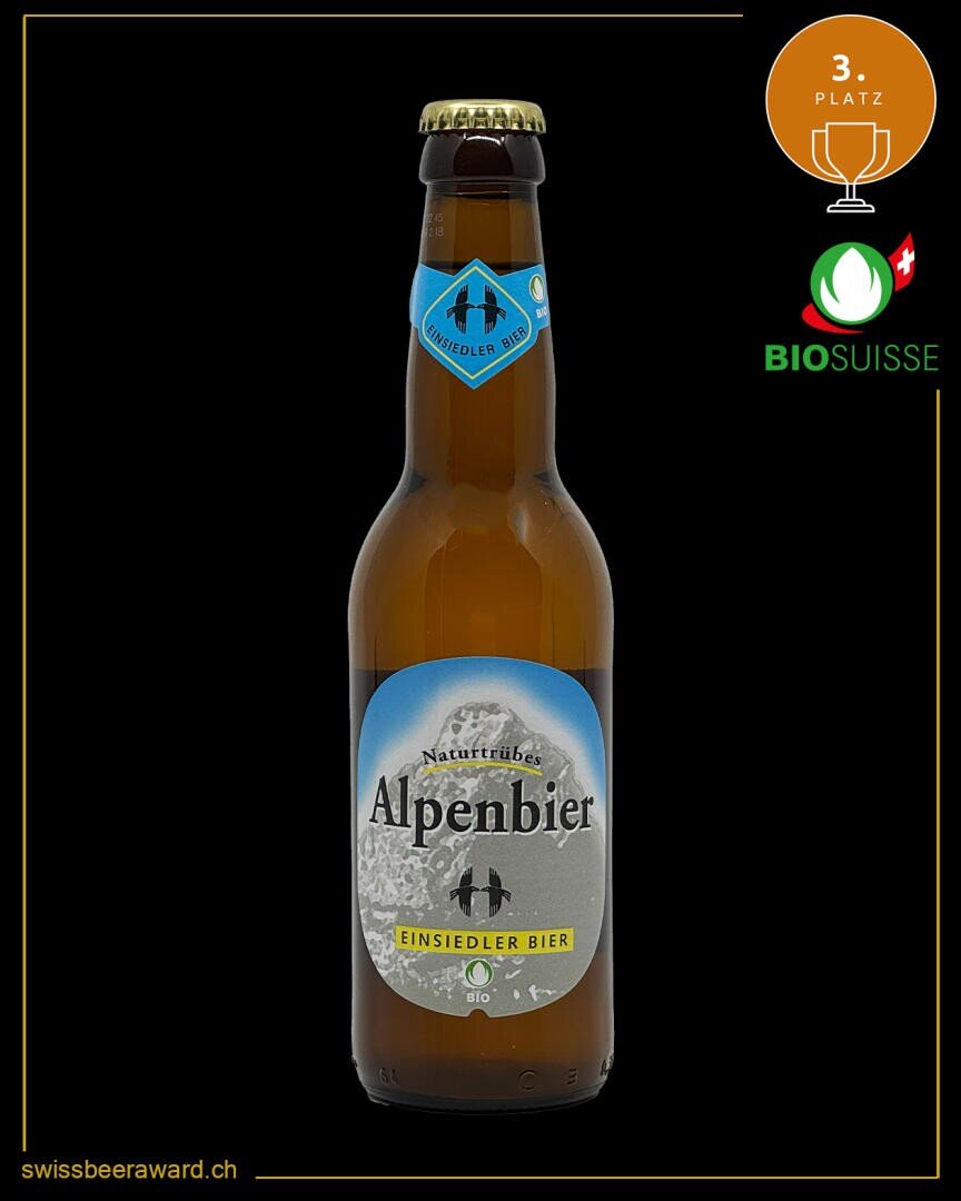 Eine braune Glasflasche Einsiedler Alpenbier mit einem blau-silbernen Etikett auf schwarzem Hintergrund. In den Ecken befinden sich die goldene Plakette, das Logo von Bio Suisse und der Link swissbeeraward.ch.
