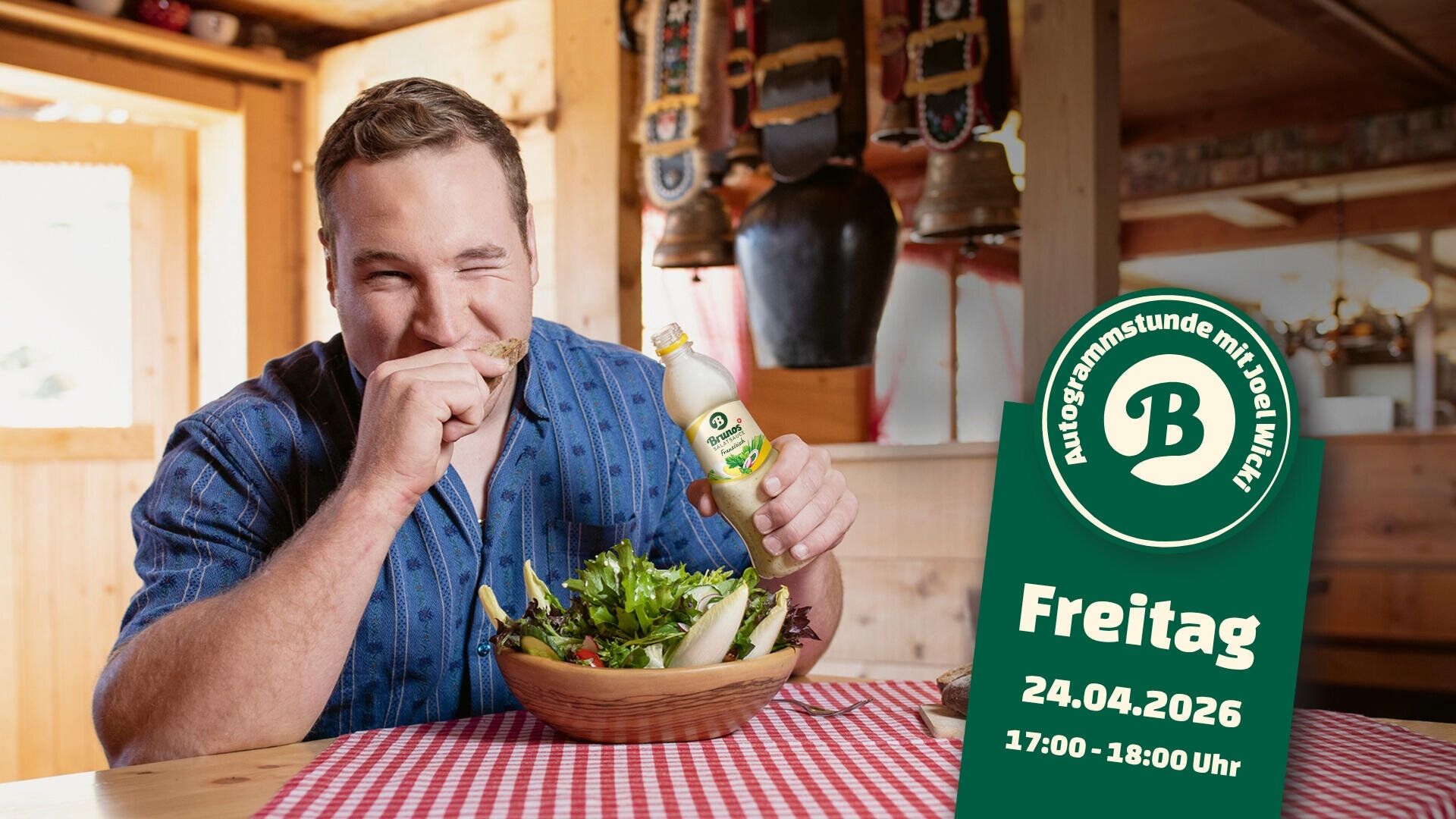 Ein Mann in einem blauen Hemd sitzt an einem Holztisch, isst Salat, hält eine Flasche Salatsoße in der Hand und lächelt. Ein grünes Schild kündigt eine Veranstaltung am Freitag, 24.04.2026, von 17:00-18:00 Uhr, mit einem Logo und deutschem Text an.
