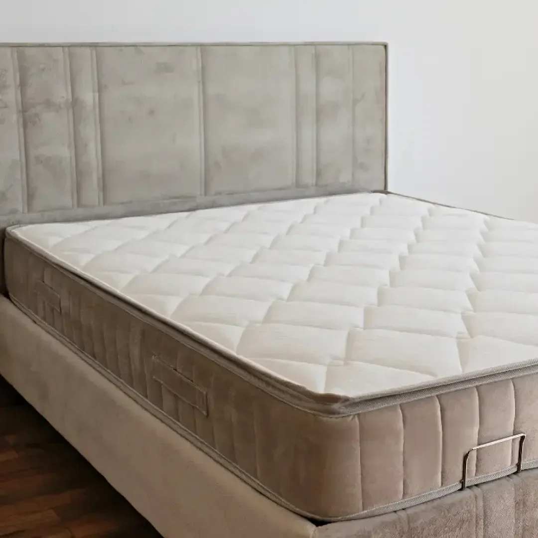 Ein beigefarbenes gepolstertes Bett mit einer hellen, gesteppten Matratze in einem minimalistischen Schlafzimmer auf einem Holzboden.