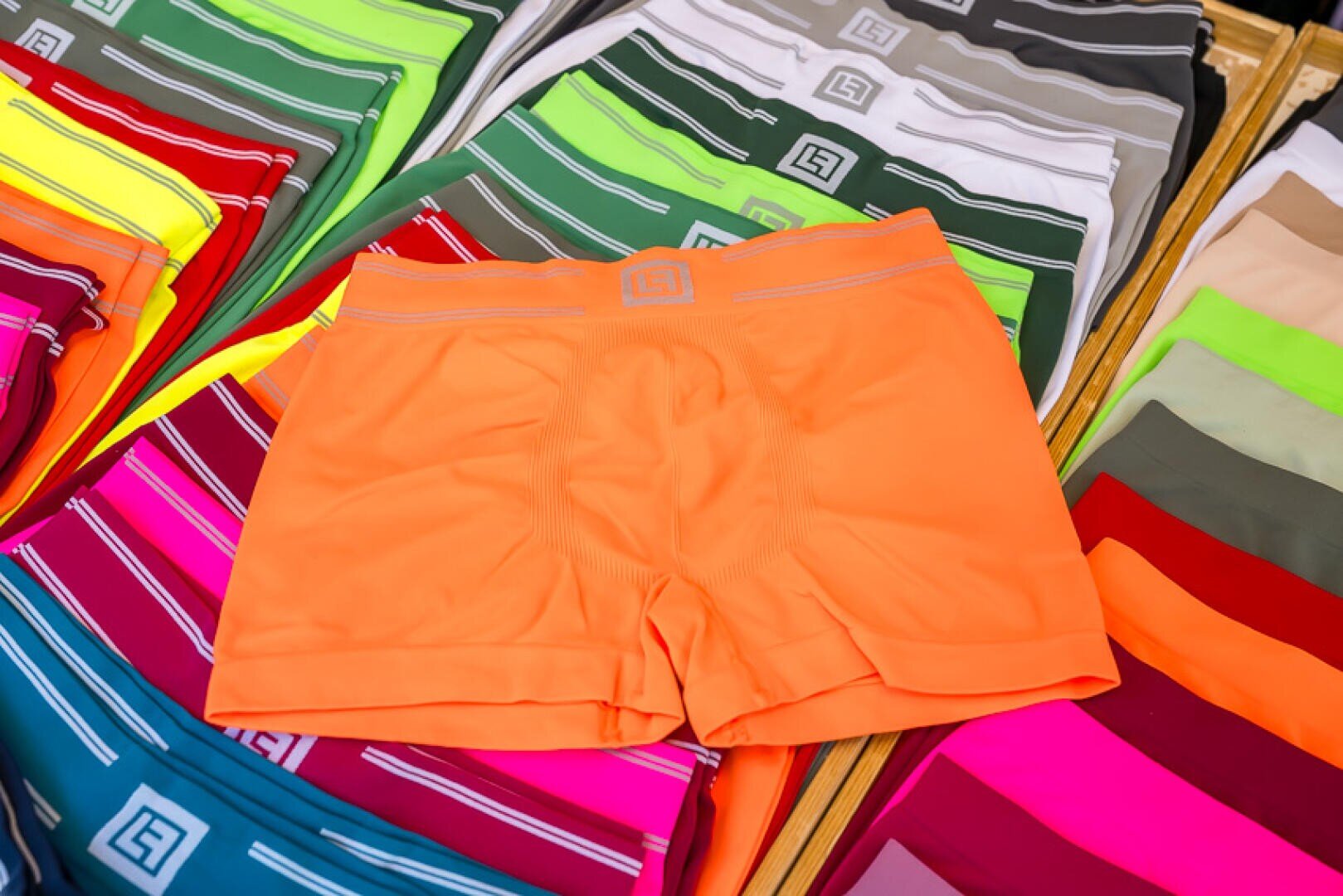 Ein Paar leuchtend orangefarbene Herren-Boxershorts, die auf ordentlich angeordneten Stapeln bunter Unterwäsche in verschiedenen Farbtönen und Mustern ausgestellt sind.