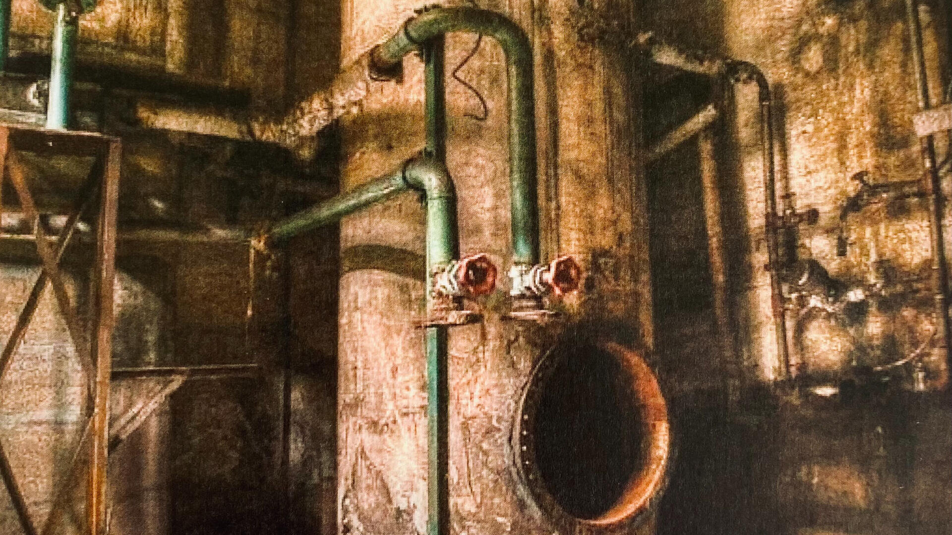 Ein verrostetes industrielles Interieur mit gealterten Metallrohren, Ventilen und Maschinen, die an großen zylindrischen Strukturen befestigt sind, die vor einer abgenutzten, verfärbten Wand stehen.