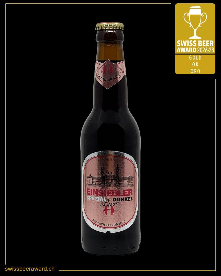 Eine Flasche Einsiedler Spezial Dunkel mit rosafarbenem Etikett steht mittig auf einem schwarzen Hintergrund. In der oberen rechten Ecke ist eine goldene Plakette des Swiss Beer Award 2026-28 zu sehen.