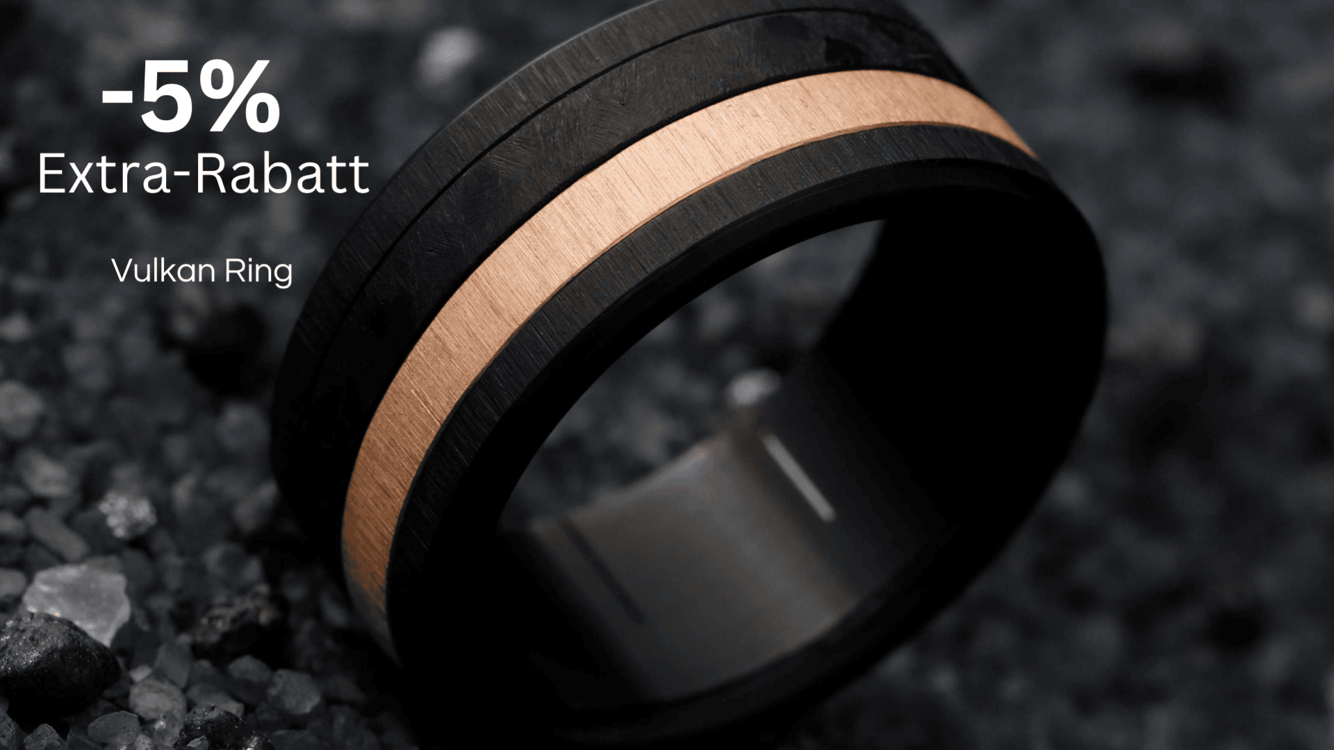 Schwarzer und roségoldfarbener Ring auf dunklen Kieselsteinen mit der Aufschrift: -5 % Extra-Rabatt Vulkan-Ring..
