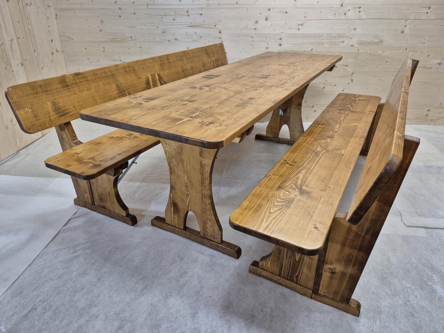 Ein Esstisch aus Holz mit zwei langen Bänken und einer kurzen Bank, alle aus dem gleichen Holz, in einem Raum mit hellen Holzwänden und -böden.