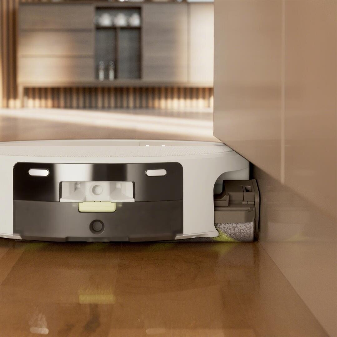 Ein weißer Staubsaugerroboter fährt an der Kante eines Holzbodens entlang und reinigt dicht an einer Wand in einem modernen, gut beleuchteten Raum.