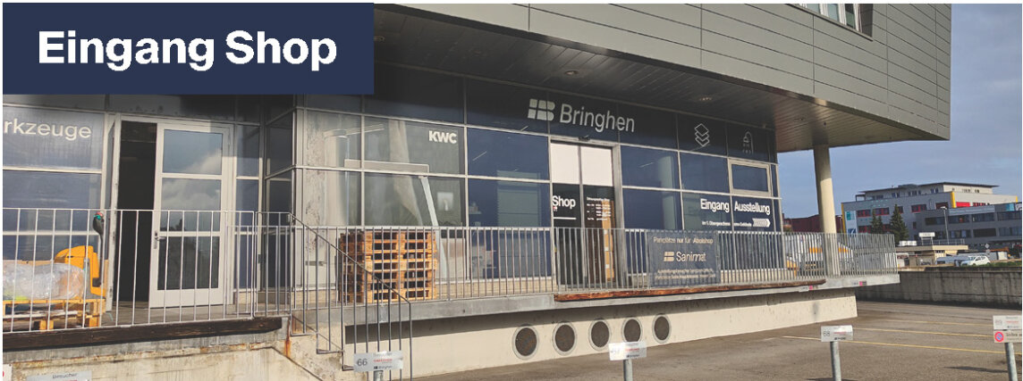 Ein modernes Gebäude mit großen Glasfenstern und einem Schild mit der Aufschrift "Eingang Shop" über dem Eingang. Das Gebäude hat eine Rampe, ein Metallgeländer und Parkplätze vor dem Gebäude.