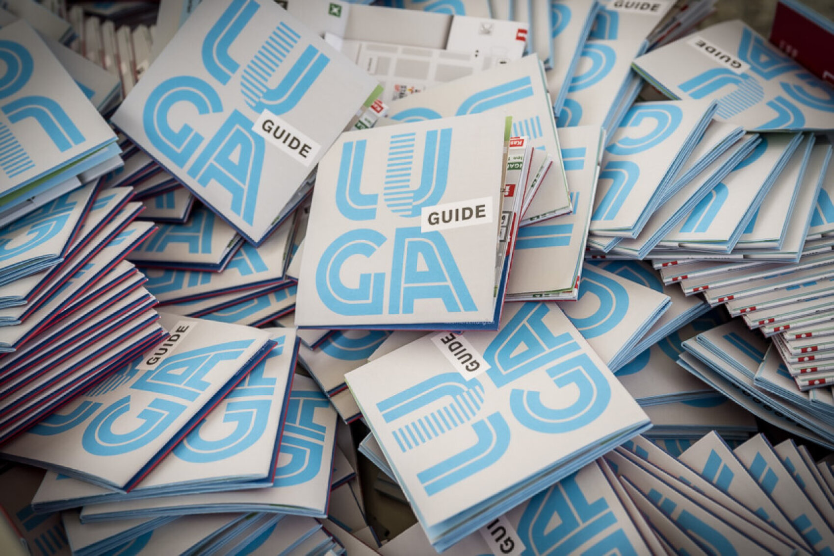 Ein großer Stapel gefalteter Broschüren mit GUIDE in fetten Buchstaben und blauen geometrischen Mustern auf den Umschlägen, die wahllos gestapelt sind.