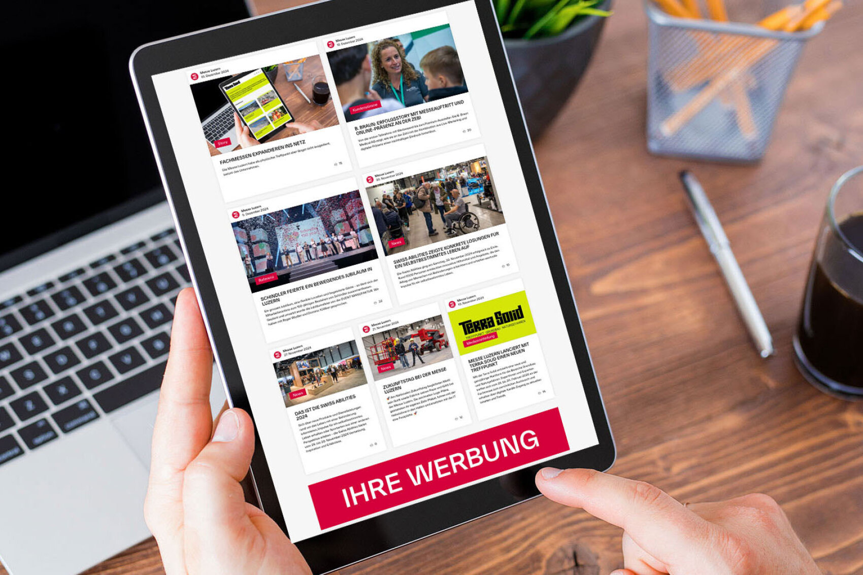 Ein Tablet zeigt eine Webseite mit mehreren Artikeln und Bildern zu Themen und Veranstaltungen der Messe Luzern. Im Hintergrund ist ein Laptop auf einem Holztisch sichtbar.